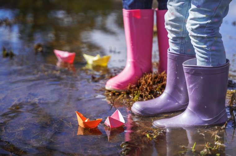 Colored paper boats,ships.Little girls in pink, purple waterproof rubber boots cheerfully jumps through puddles on street in rainy weather.Hello spring,autumn.Children’s fun in fresh air after rain Colored paper boats,ships.Little girls in pink, purple waterproof rubber boots cheerfully jumps through puddles on street in rainy weather.Hello spring,autumn.Children’s fun in fresh air after rain